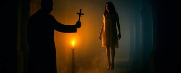 escena de exorcismo y posesión demoníaca. Sacerdote alza un crucifijo ante mujer que levita en un pasillo oscuro de iglesia.